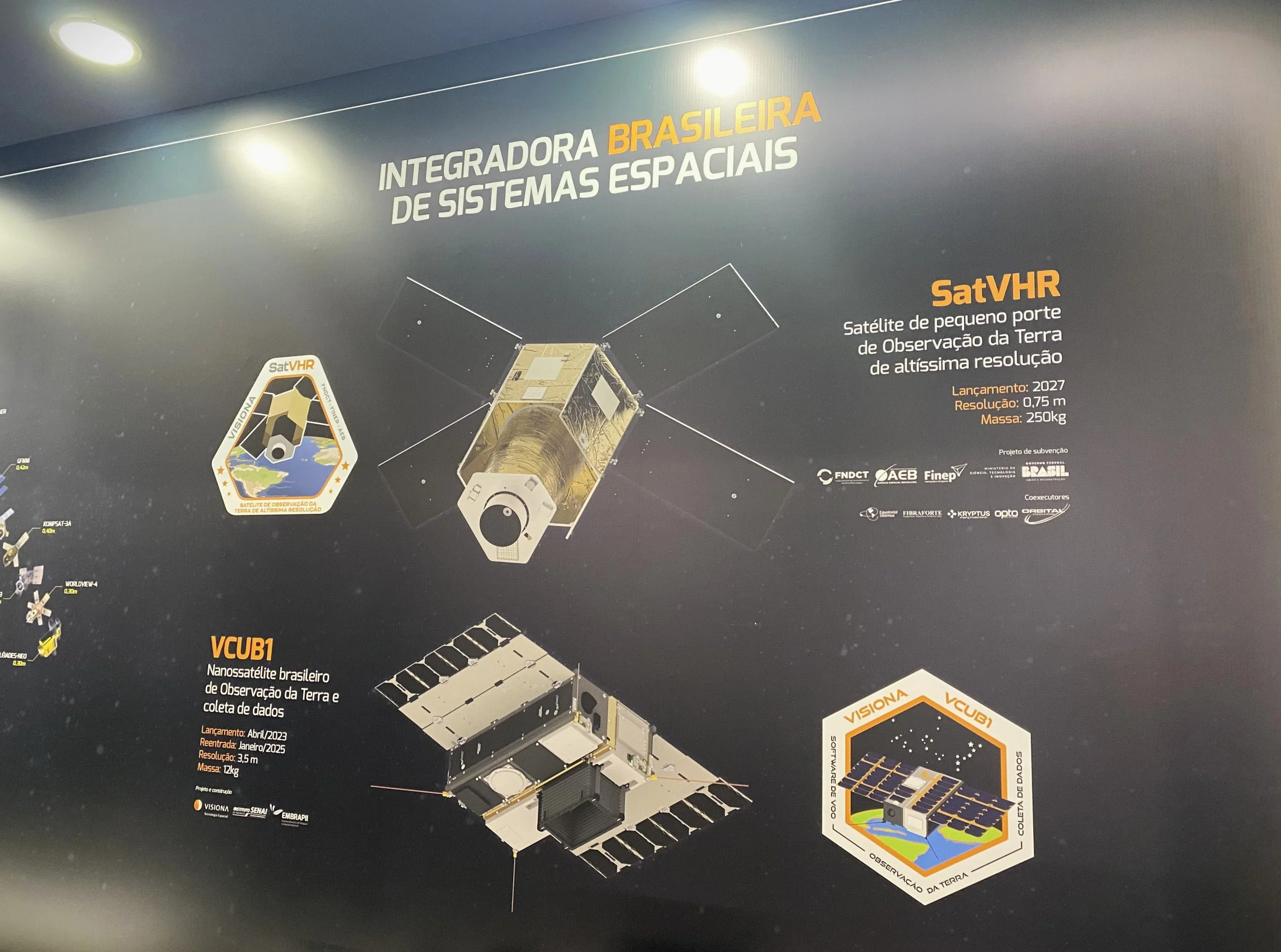Design gráfico do SatVHR, vencedor do Prêmio Finep, aplicado em uma parede, com um pequeno texto ao lado: Satélite de Pequeno Porte de Observação da Terra em altíssima resolução.